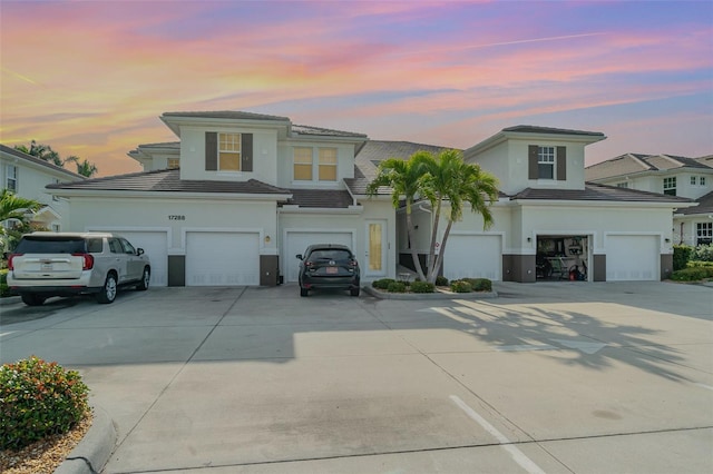 view of front facade with driveway, an attached garage, stucco siding, a garage, and a tiled roof