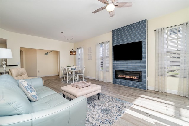 living room with ceiling fan, baseboards, a large fireplace, and wood finished floors