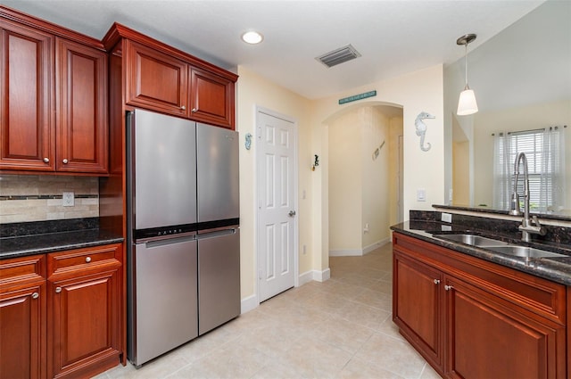 kitchen with visible vents, arched walkways, freestanding refrigerator, a sink, and backsplash