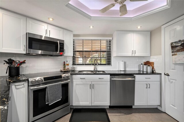 kitchen featuring white cabinets, stainless steel appliances, a raised ceiling, and a sink