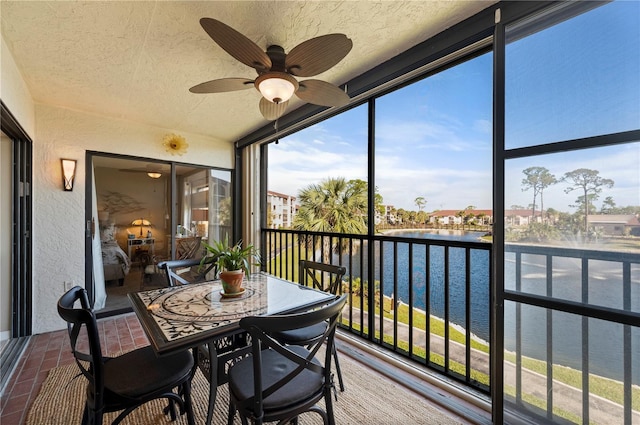 sunroom with ceiling fan and a water view