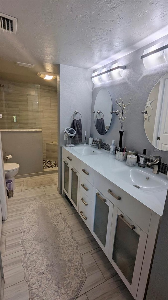 full bath featuring visible vents, a walk in shower, a sink, a textured ceiling, and double vanity