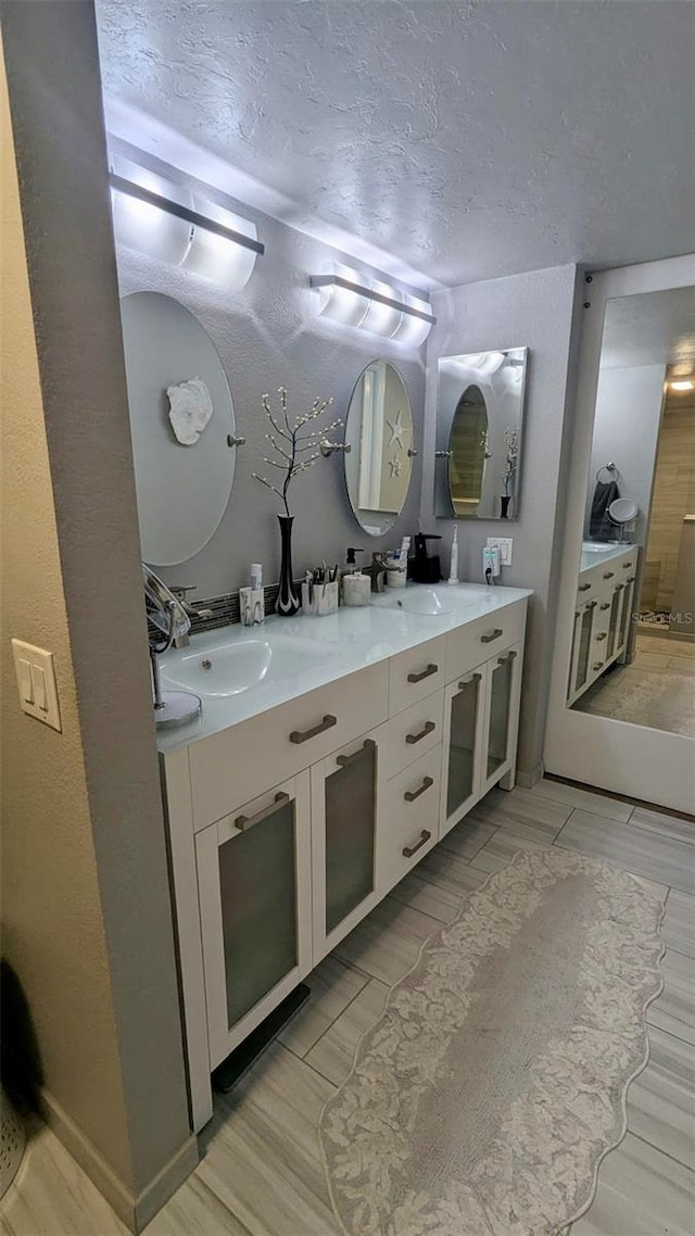 bathroom with double vanity, a textured ceiling, wood tiled floor, and a sink