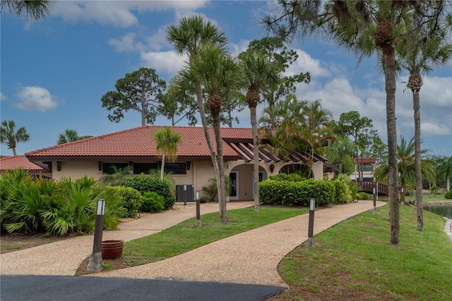 view of front facade with a front lawn, central air condition unit, a tile roof, and stucco siding