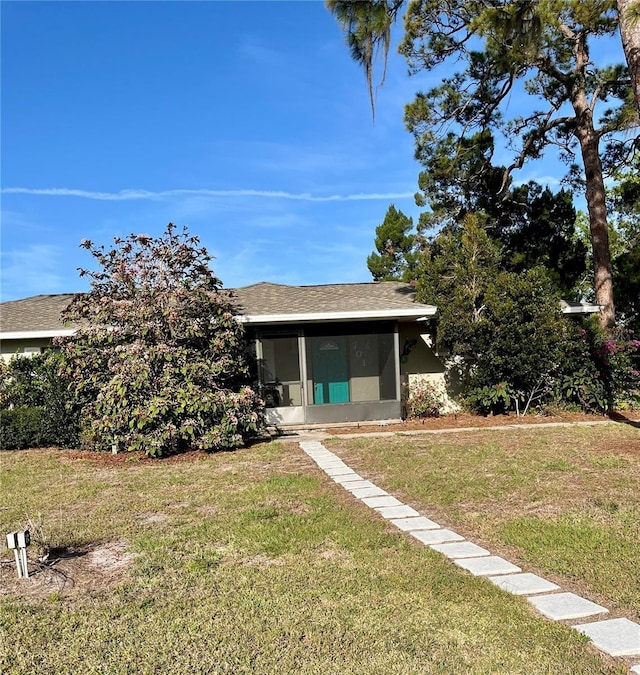 view of front of home featuring a sunroom, roof with shingles, a front lawn, and stucco siding