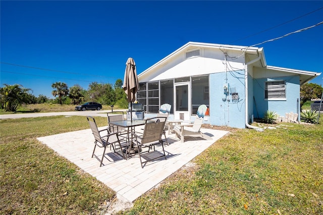 back of property with a sunroom, stucco siding, a patio, and a yard