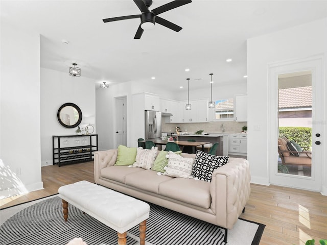 living room featuring light wood-type flooring, baseboards, a ceiling fan, and recessed lighting