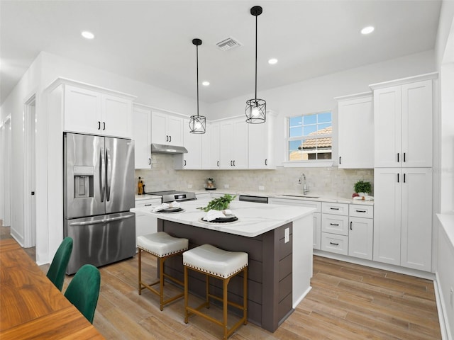 kitchen featuring appliances with stainless steel finishes, white cabinets, a sink, and under cabinet range hood