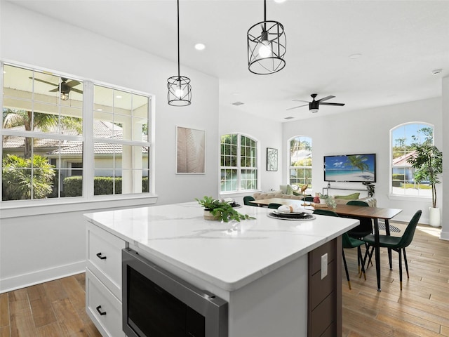 kitchen with dark wood finished floors, stainless steel microwave, open floor plan, ceiling fan, and plenty of natural light