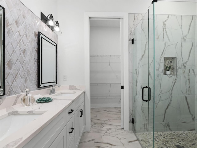 bathroom featuring marble finish floor, a marble finish shower, double vanity, a spacious closet, and a sink