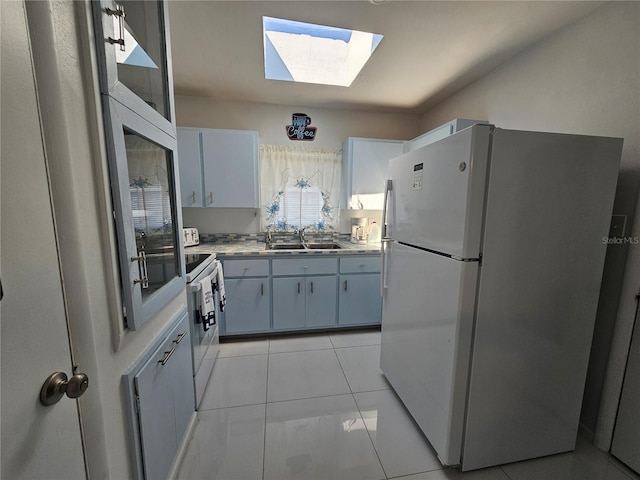 kitchen featuring white appliances, a skylight, light countertops, a sink, and light tile patterned flooring