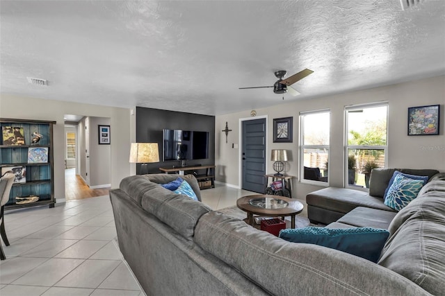 living room featuring baseboards, visible vents, a ceiling fan, a textured ceiling, and light tile patterned flooring