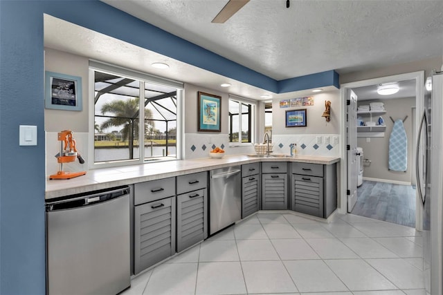 kitchen featuring stainless steel appliances, tasteful backsplash, gray cabinets, light tile patterned flooring, and a sink