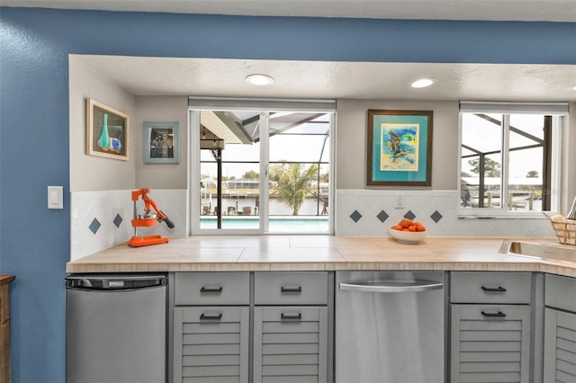 kitchen featuring dishwasher, backsplash, gray cabinetry, stainless steel dishwasher, and a sink