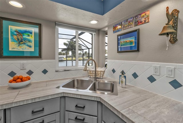 kitchen with a textured ceiling, a textured wall, gray cabinetry, a sink, and light countertops