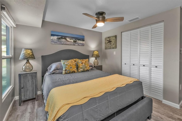 bedroom with a closet, visible vents, a ceiling fan, wood finished floors, and baseboards