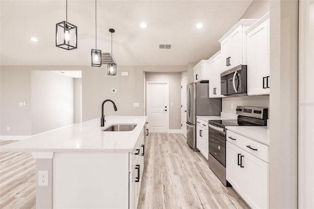 kitchen with stainless steel appliances, a sink, white cabinetry, light wood-style floors, and a center island with sink