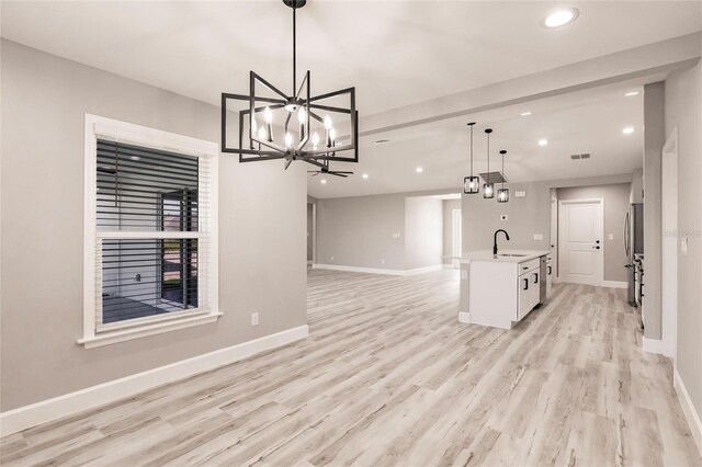 kitchen with light wood finished floors, baseboards, open floor plan, light countertops, and a sink