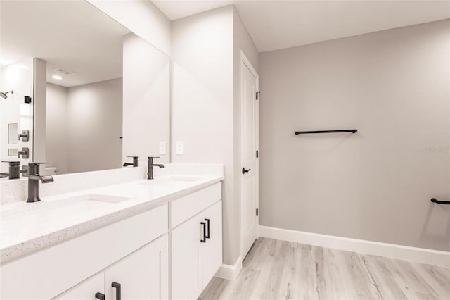 bathroom featuring double vanity, wood finished floors, a sink, and baseboards