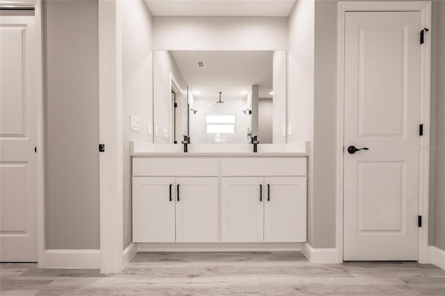 full bath featuring a sink, double vanity, wood finished floors, and baseboards