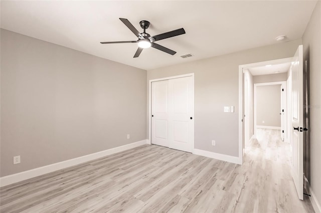 unfurnished bedroom featuring ceiling fan, light wood-style flooring, visible vents, baseboards, and a closet