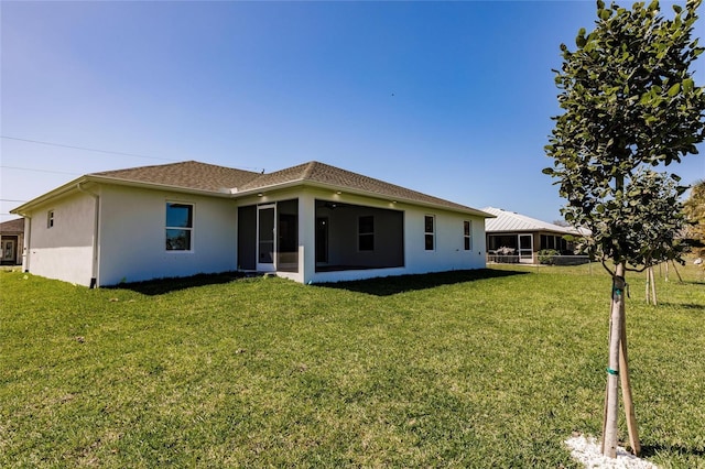 rear view of property featuring a sunroom, a lawn, and stucco siding