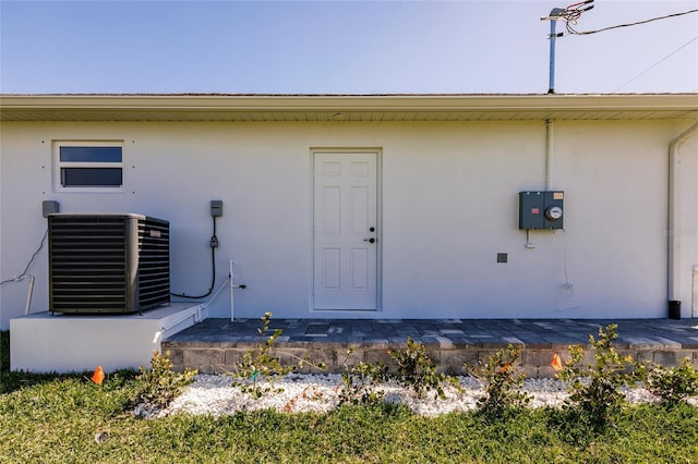 view of exterior entry with central AC unit and stucco siding