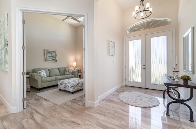 entryway with light wood finished floors, baseboards, ceiling fan with notable chandelier, french doors, and a towering ceiling