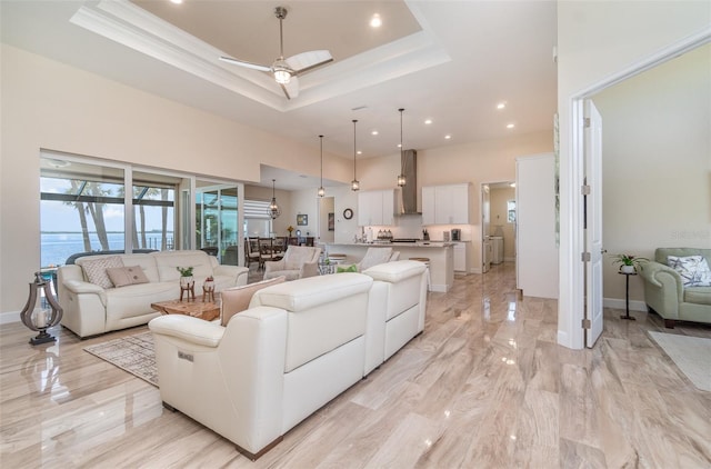 living room featuring baseboards, a raised ceiling, a high ceiling, and ornamental molding