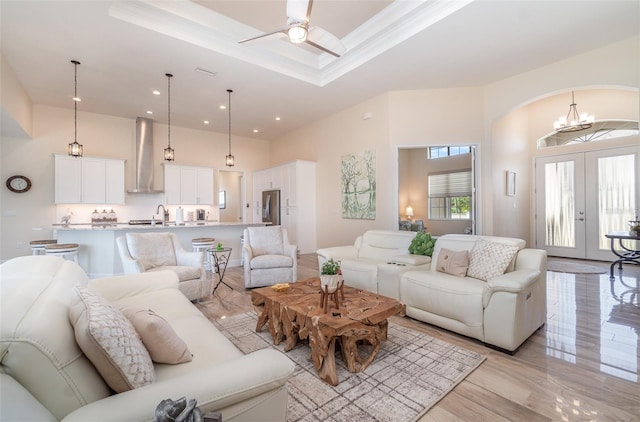 living room with ceiling fan with notable chandelier, recessed lighting, french doors, a raised ceiling, and a towering ceiling