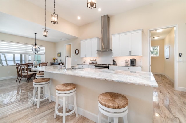 kitchen with tasteful backsplash, gas range, a wealth of natural light, white cabinetry, and wall chimney exhaust hood