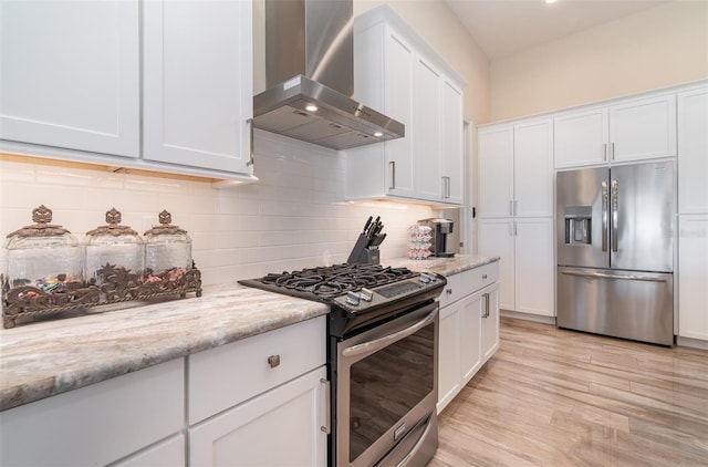 kitchen featuring light wood-type flooring, tasteful backsplash, white cabinetry, stainless steel appliances, and wall chimney exhaust hood