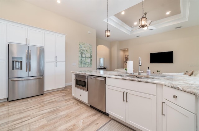 kitchen with a tray ceiling, light wood-style floors, arched walkways, stainless steel appliances, and a sink