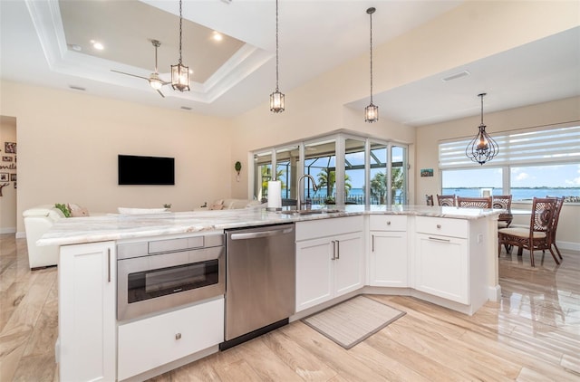 kitchen featuring light stone countertops, a sink, dishwasher, a raised ceiling, and open floor plan