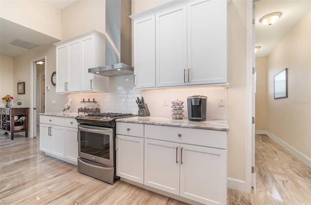 kitchen featuring decorative backsplash, white cabinetry, stainless steel gas range, and wall chimney range hood