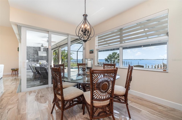 dining room with light wood finished floors, baseboards, a water view, and ceiling fan with notable chandelier