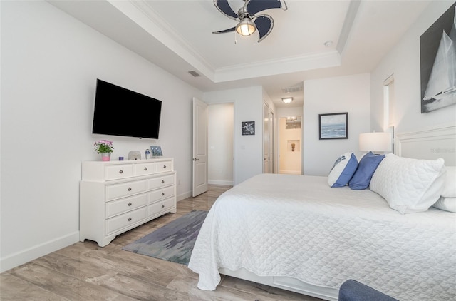 bedroom featuring visible vents, baseboards, light wood-type flooring, and a tray ceiling