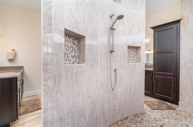 full bathroom featuring a tile shower, vanity, and baseboards