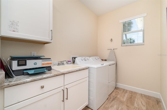 laundry area featuring washing machine and clothes dryer, baseboards, light wood-type flooring, cabinet space, and a sink