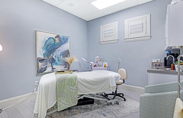 bedroom with a paneled ceiling, a sink, baseboards, and wood finished floors