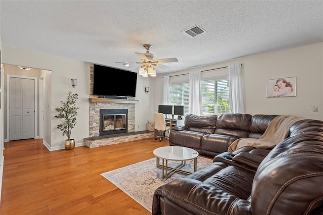 living room featuring visible vents, a stone fireplace, wood finished floors, a textured ceiling, and a ceiling fan