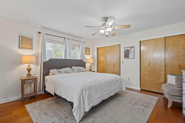 bedroom with a textured ceiling, baseboards, two closets, and hardwood / wood-style flooring