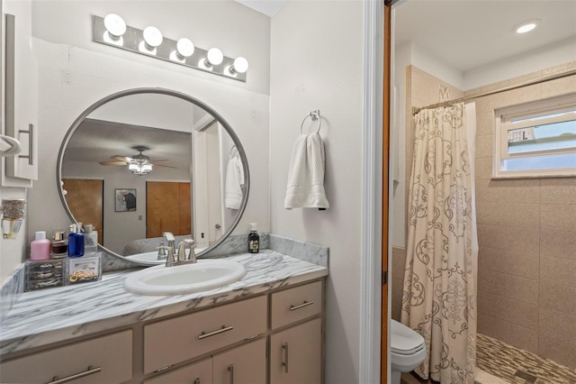 bathroom with tiled shower, toilet, vanity, and ceiling fan