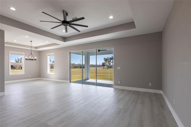 spare room with light wood finished floors, baseboards, a raised ceiling, and ceiling fan with notable chandelier