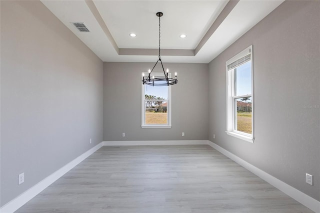 unfurnished dining area featuring a tray ceiling, a notable chandelier, light wood finished floors, visible vents, and baseboards