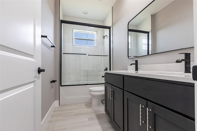 bathroom featuring shower / bath combination with glass door, toilet, vanity, wood finished floors, and baseboards