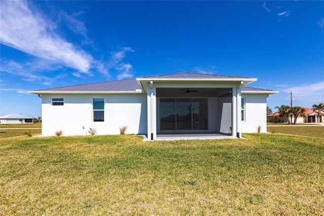 rear view of property featuring metal roof, a sunroom, a ceiling fan, a yard, and stucco siding