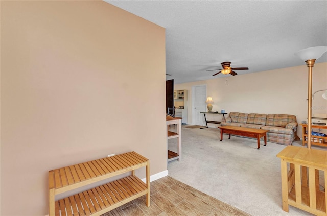 living area featuring light colored carpet, a ceiling fan, baseboards, and light wood finished floors