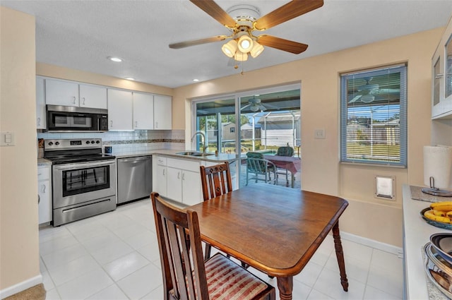 kitchen with a sink, backsplash, white cabinetry, appliances with stainless steel finishes, and ceiling fan