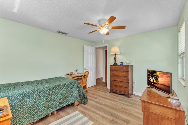 bedroom with a ceiling fan, baseboards, visible vents, light wood-style flooring, and a textured ceiling